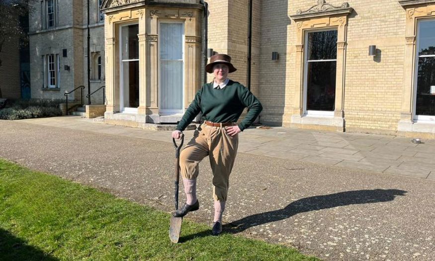 Visitor Host, Rachel, dressed as a Land Girl stood outside Chelmsford Museum with her foot on a spade. 