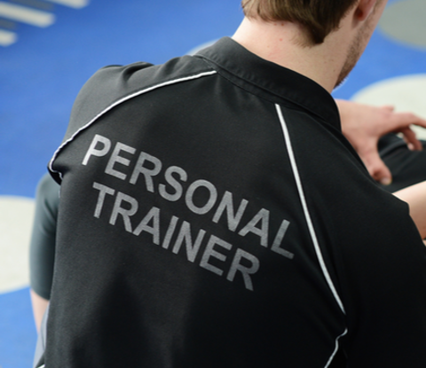 Man wearing t-shirt saying 'Personal trainer' helping women who is doing crunches on a exercise ball