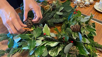 A closeup of hands working on a wreath made of fresh greenery. 