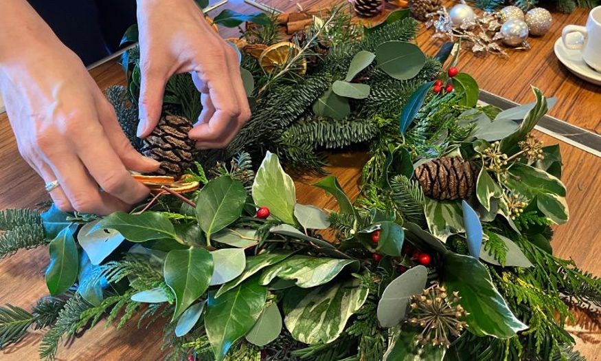 A closeup of hands working on a wreath made of fresh greenery. 