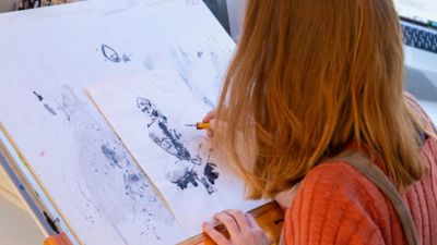 A woman drawing on a white piece of paper with black ink. 