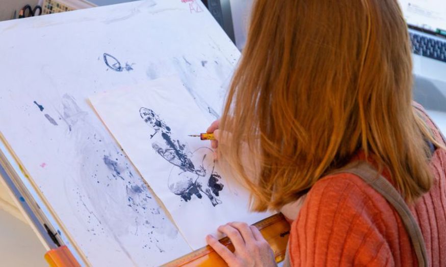 A woman drawing on a white piece of paper with black ink. 