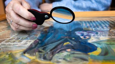 A close up of a woman looking at a painting with a magnifying glass. 