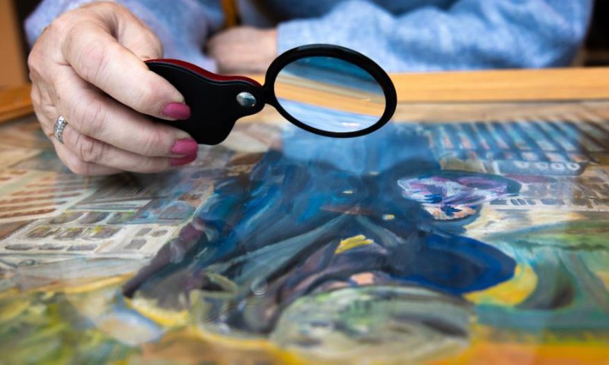 A close up of a woman looking at a painting with a magnifying glass. 