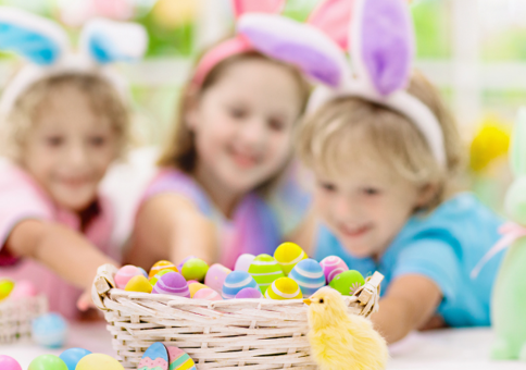 Children at an Easter party reaching out to a mini basket full of mini Easter eggs.