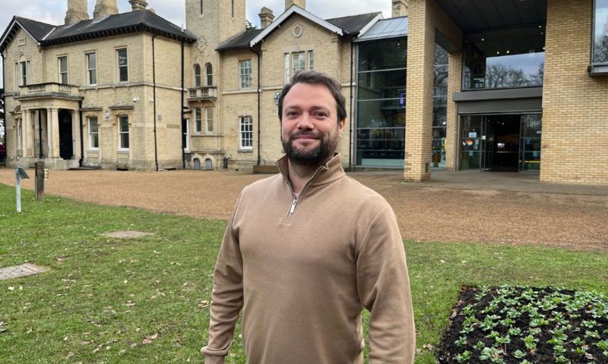 A man standing on the lawn outside Chelmsford Museum smiles at the camera. 