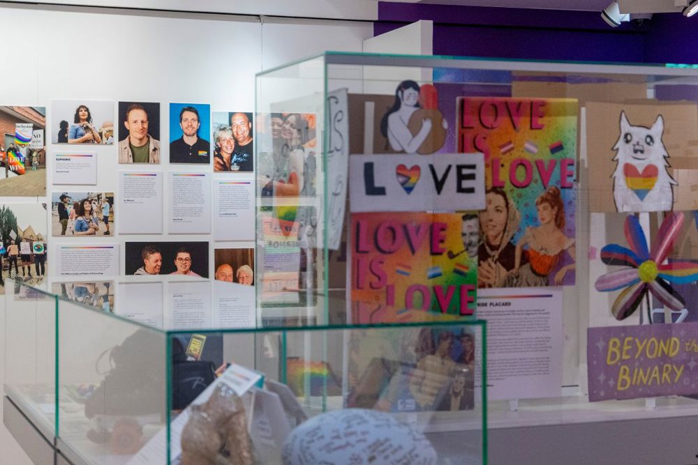 The Behind the Rainbow exhibition with portraits on the wall and signs in a display case. 