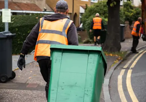 Man in an orange high vis pulling a green wheelie bin