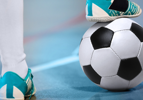 Person's foot rest on football on indoor pitch