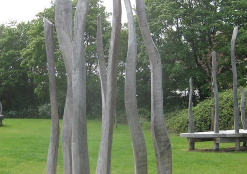 Three large wooden platforms with tall, wavy posts sited in green space