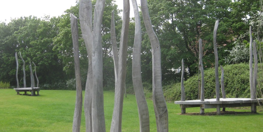 Three large wooden platforms with tall, wavy posts sited in green space