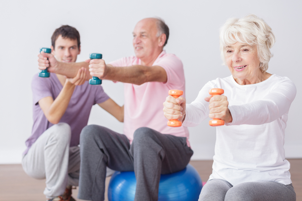 Man coaching older people who are sitting on exercise balls and using hand weights