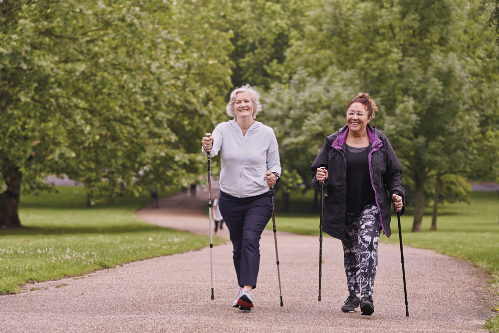 Two mature ladies walking along footpath and using walking poles