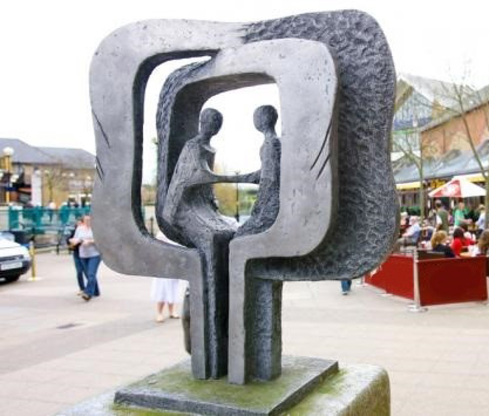 A sculpture of two people sitting, facing each other and holding hands, both surrounded by two square frames, commemorating the 10 year friendship between Chelmsford and Backnang.