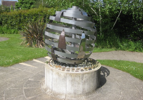 Steel globe sculpture with stylized flames, sitting on a plinth in a public park