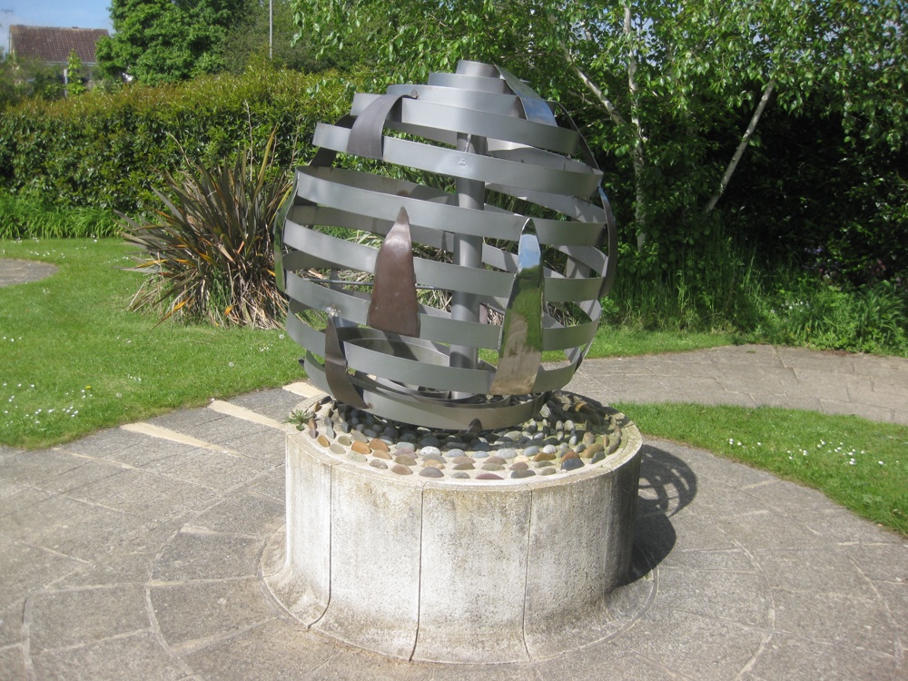 Steel globe sculpture with stylized flames, sitting on a plinth in a public park