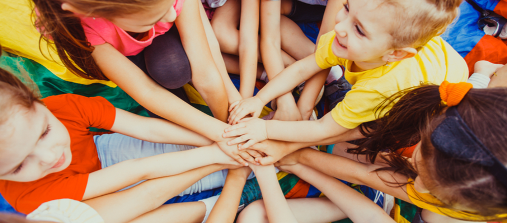 Group of children in a circle, putting their hands together in the middle