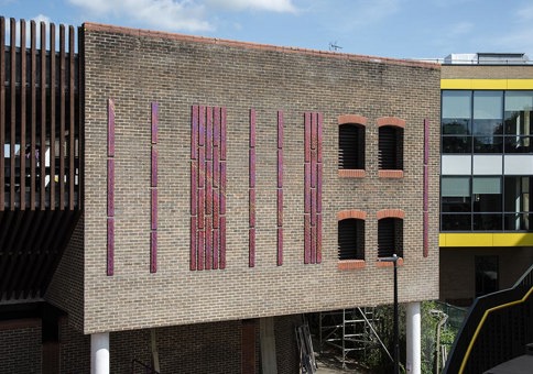 Tall, vertical, copper panels on outside brick wall of car park