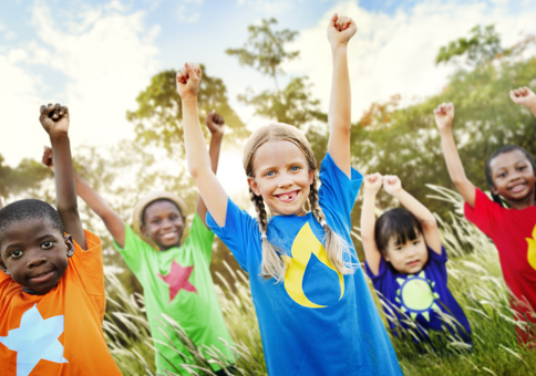 Group of happy young children smiling with their arms in the air, wearing brightly coloured t-shirts